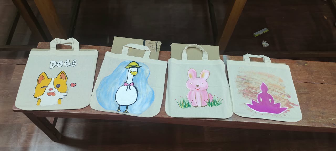 Four finished tote bags painted with a dog, a goose, a bunny and a lotus flower