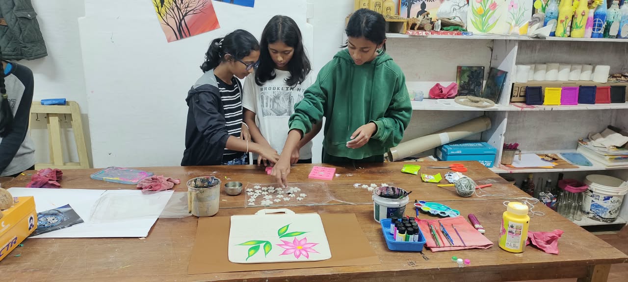 Three students working together to add finishing touches to a painted tote bag