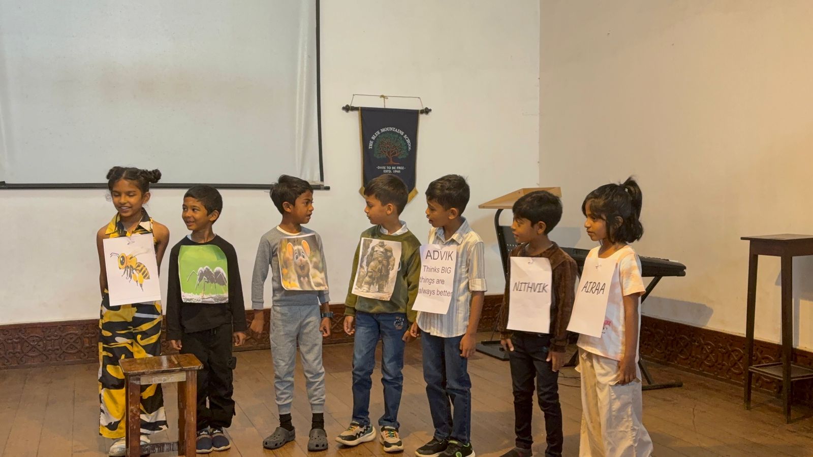 Students dressed as a bee, an ant, a wolf and a bear face Advik, Nithvik and Airaa on stage during the assembly skit