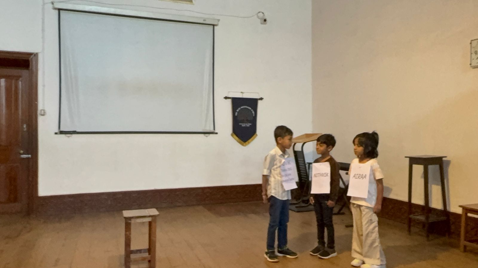 Advik, Nithvik and Airaa stand on stage as the assembly skit begins