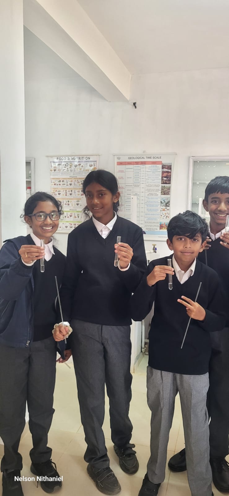 Four Grade 7 students smiling and holding up their test tubes of milky lime water at bms
