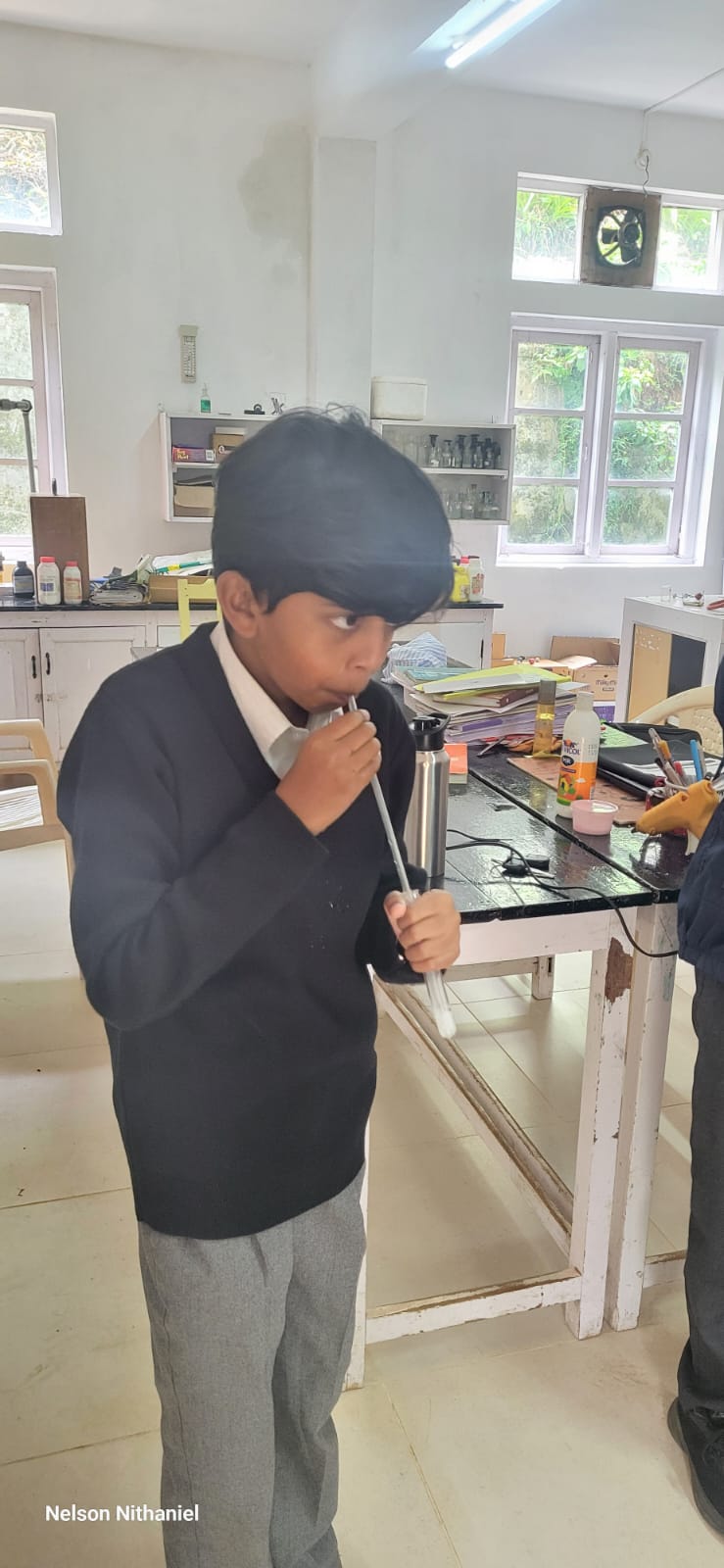 A student blowing exhaled air through a straw into a test tube of lime water